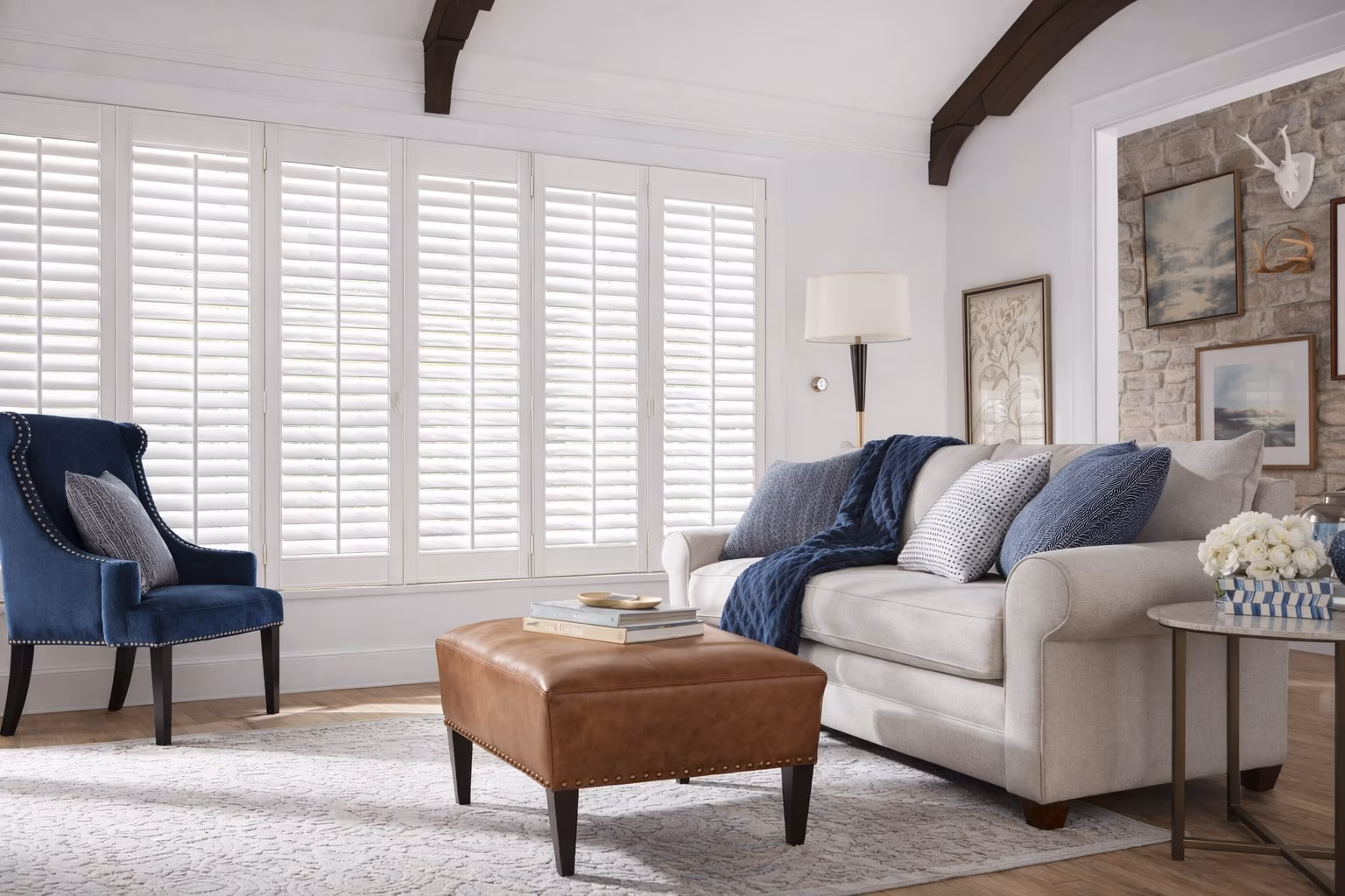 Hunter Douglas NewStyle Hybrid Shutters spanning a wide window wall in a modern farmhouse living room with stone accent wall and exposed beams, installed by La Grange Window Coverings